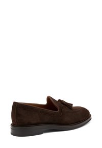 Mocassini in suede marrone con punta rotonda, dettaglio con frange e cuciture a contrasto. Presentano una suola piatta in gomma e una fodera interna liscia.