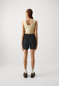 Knit cream tank top with scalloped edges, paired with dark gray textured shorts. Brown shoes with white socks complete the outfit.