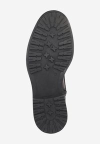 Semelle de chaussure en caoutchouc noir avec une surface texturée et motif comprenant plusieurs rainures d'adhérence et formes surélevées pour une meilleure prise.