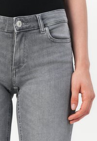 Grå denimjeans med høy midje, frontlommer, knappeåpning og en glatt tekstur. Stoffet har en subtil vaskeeffekt.