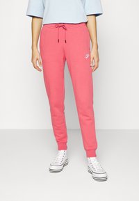 Růžové tepláky s elastickým pasem, nastavitelným stahovacím páskem a logem Nike na levém stehně. Kombinované s bílými vysokými teniskami.