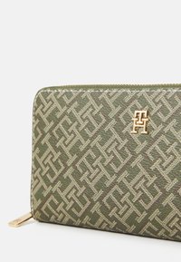 Green patterned wallet with gold hardware. Features geometric design in textured material, highlighted by logo detail on the front.