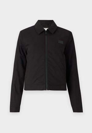 Czarna krótka kurtka z zapięciem na zamek, szpiczastym kołnierzem i długimi rękawami. Gładki materiał z minimalnymi akcentami, z małą naszywką z logo na klatce piersiowej.