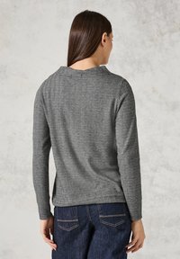 Grå långärmad topp med herringbone-textur, rund halsringning och en avslappnad passform. Kombinerad med mörka denimjeans.