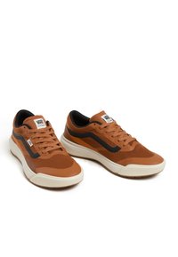 Bruna atletiska sneakers med en texturerad ovansida, svarta accenter och en vit gummisula. Funktioner inkluderar snörning och en märkes-tunga.