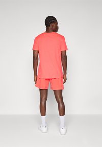 Coral short-sleeve t-shirt and matching shorts made of lightweight fabric. White sneakers and socks complete the sporty look.