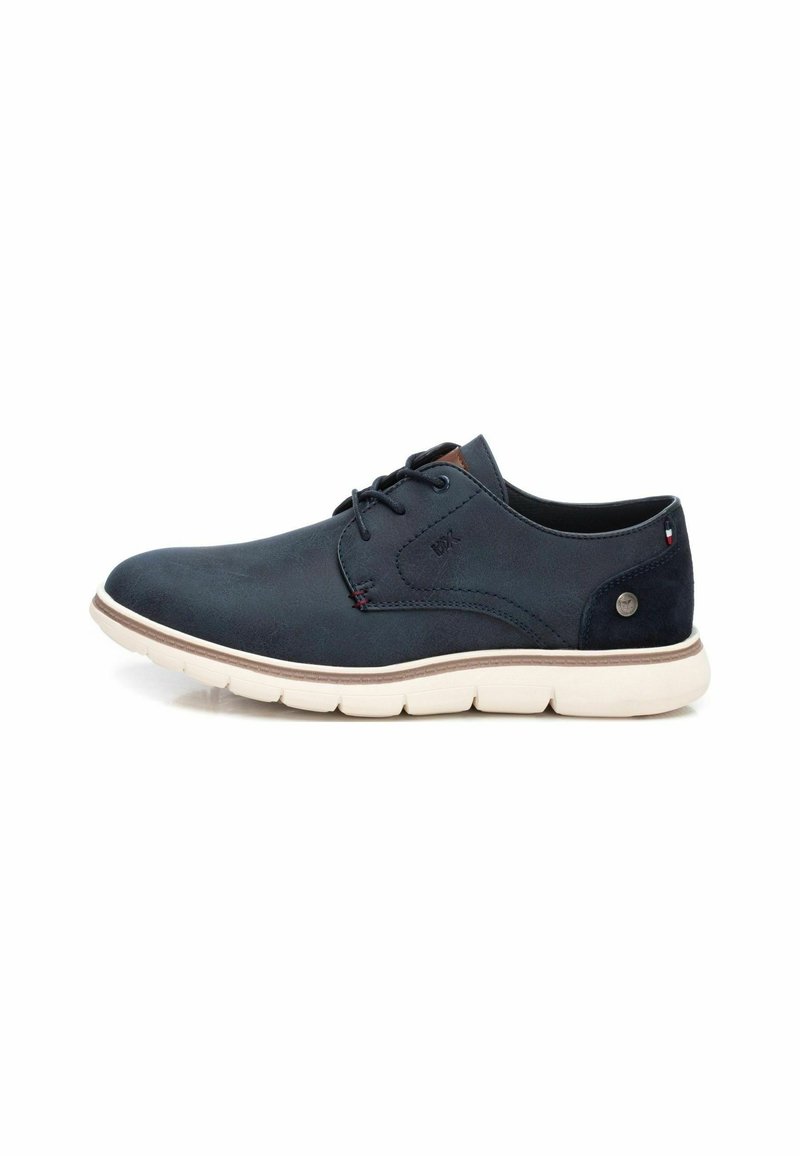 Zapato de cuero azul marino con cordones y puntera redonda, suela de goma blanca y pespuntes en tonalidad. Presenta un pequeño logo circular en el lateral.