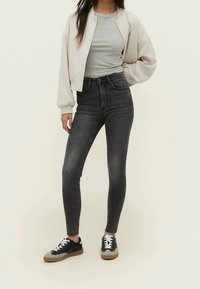 Černé skinny džíny s vysokým pasem, šedý žebrovaný top pod světle béžovou zkrácenou bomber bundou, doplněné černými a šedými teniskami.