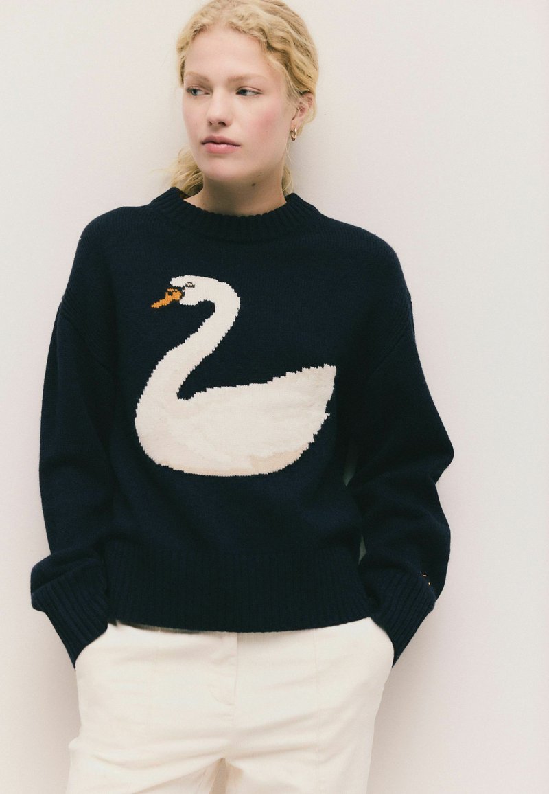 Maglione lavorato a maglia di colore blu navy con un grande design di cigno bianco sul fronte. Polsini e orlo a costine, con scollo rotondo.