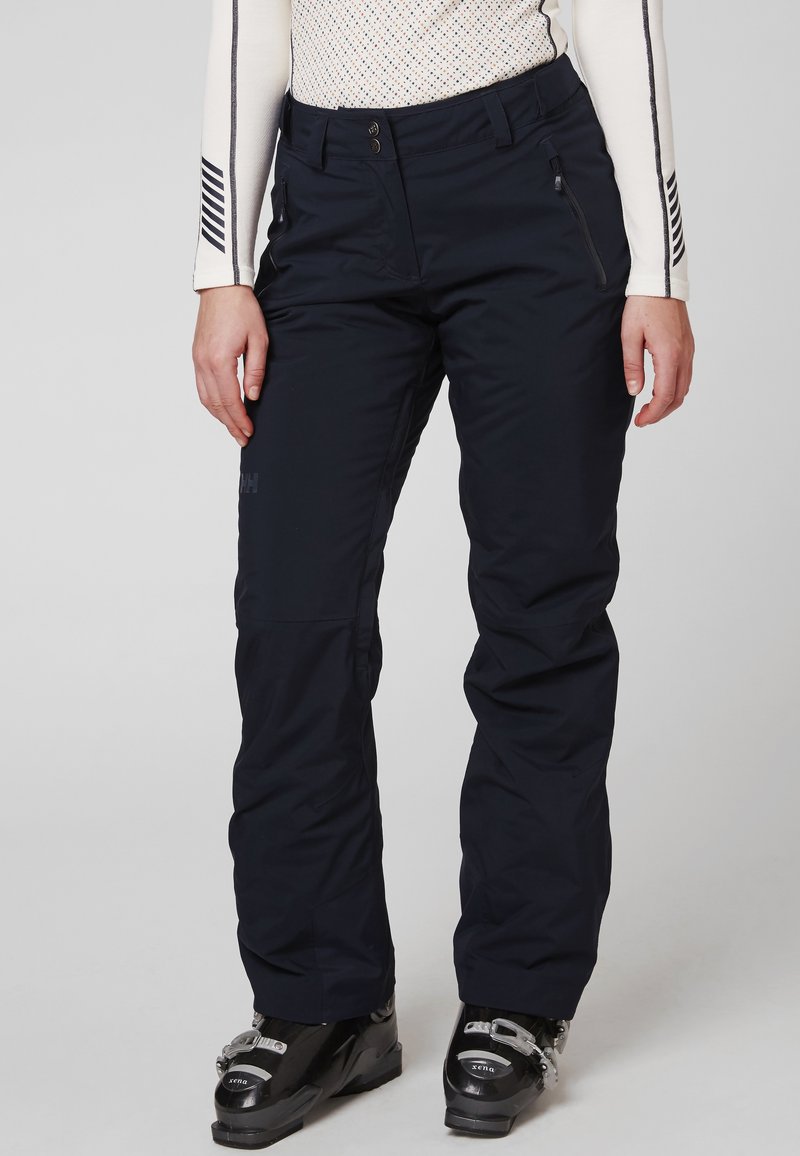 Marineblauwe skibroek met een gladde textuur, voorste drukknoopsluiting en ritszakken; gecombineerd met zwarte skibotten.