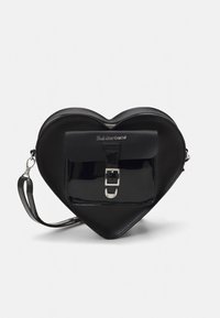 Juodos spalvos širdies formos rankinė iš lygaus ir blizgaus odos, su priekinio dangtelio sagtimi ir reguliuojamu dirželiu.