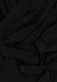 Zwarte stof heeft een zachte textuur met gedrapeerde delen en een gestrikte taille. Elastische tailleband voor aanpassing van de pasvorm.