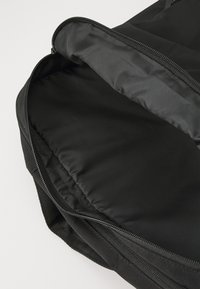 Intérieur d'un sac à dos en tissu noir avec une fermeture éclair, présentant un revêtement lisse et sans texture et un compartiment spacieux. Aucun motif ni accent visible.