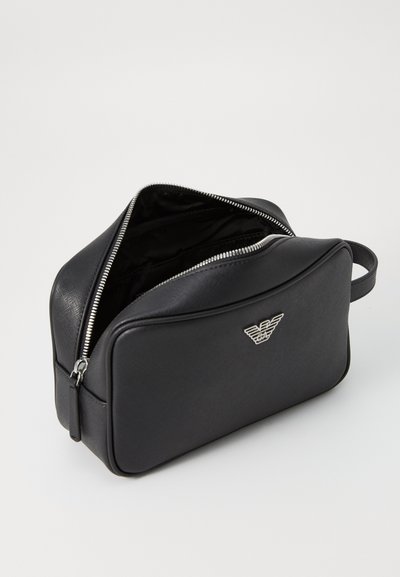 Black leather cosmetic bag with a zip closure, smooth texture, and an embossed logo on the front. Includes a side handle for carrying.