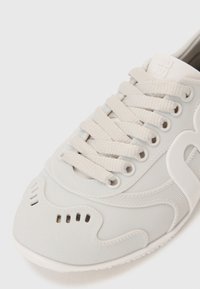 Light gray sneakers with textured plastic material, featuring prominent stitching, tonal laces, and ventilation holes on the toe cap.
