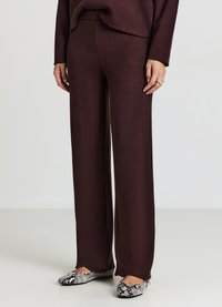 Pantaloni bordeaux a gamba larga in tessuto morbido, con una texture liscia. Abbinati a ballerine nere e bianche con motivo a fantasia.
