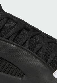 Scarpa da ginnastica nera con una parte superiore testurizzata e pannelli in rete, lacci piatti e suola sintetica. Il design enfatizza traspirabilità e flessibilità.