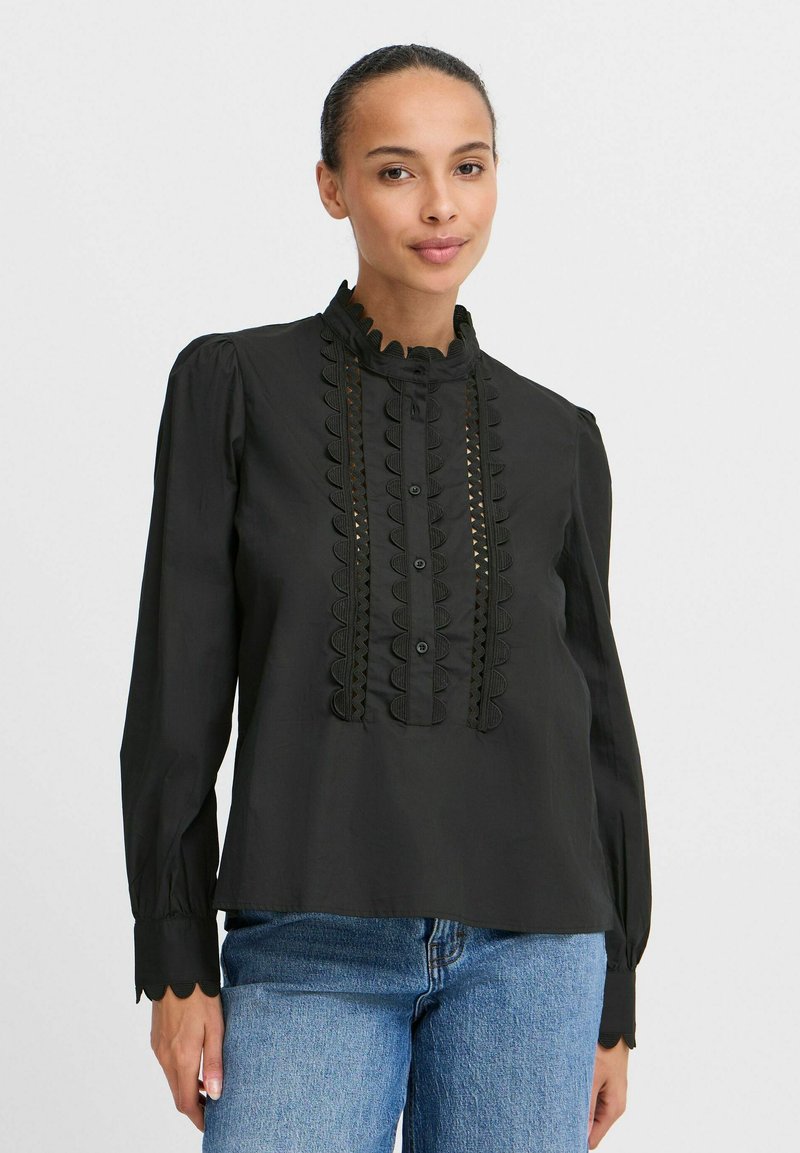 Black long-sleeve blouse with scalloped collar, pintuck detailing, and decorative buttons. Made of smooth fabric, paired with blue jeans.