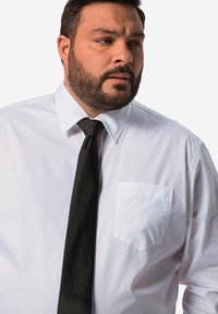 Biała koszula z długim rękawem, z kołnierzykiem zapinanym na guziki i kieszonką na lewej piersi, w połączeniu z czarnym krawatem, prezentowana na osobie z brodą.
