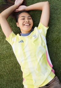 Gul och vit sporttröja med prickigt mönster, rosa accenter och en Adidas-logotyp. Texturerad tyg med rundad nackdesign.