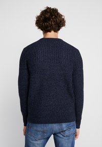 Laivaston sininen neulepusero, jossa on teksturoitu, resorikuvio ja pyöreä pääntie. Pitkät hihat ja rento istuvuus, helmassa vyötärölle ulottuva pituus.