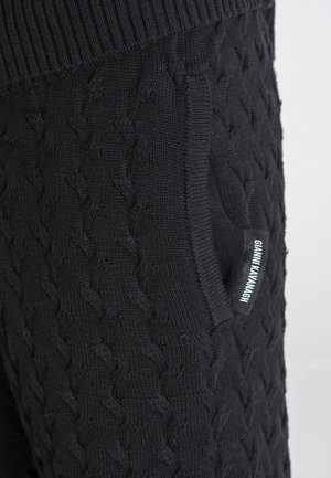 Pantalones deportivos negros de punto con textura de trenzado, cintura acanalada, bolsillo lateral y una pequeña etiqueta de marca en el bolsillo.
