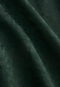 Tissu vert foncé avec des motifs floraux texturés subtils et des plis doux créant des ombres et des reflets délicats.