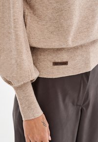 Beżowy sweter dzianinowy z bufiastymi rękawami i ściągaczami; posiada brązową metkę z napisem "blue shadow" na pasie.