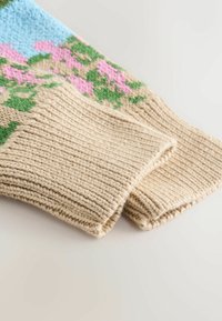 Beige gestrickte Pulloverwulstabschlüsse haben eine gerippte Struktur mit bunten Blumenmustern in Rosa und Grün vor einem hellblauen Hintergrund.