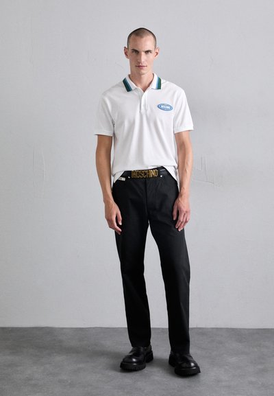 Vit polo skjorta med gröna och blå krage ränder, mörka byxor och svarta skor. Har en guld "MOSCHINO" bälte spänne.