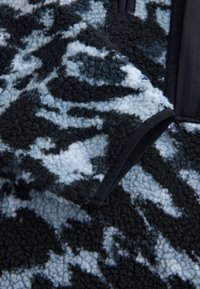 Fleece-stof in tinten zwart en blauw met abstracte patronen, voorzien van een getextureerd oppervlak en afgewerkte randen. Zacht, warm materiaal.