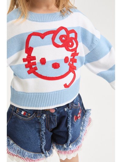 Enfant portant un pull rayé bleu et blanc avec un grand visage rouge de Hello Kitty, et un short en jean aux bords effilochés orné de patches en forme de nœuds.