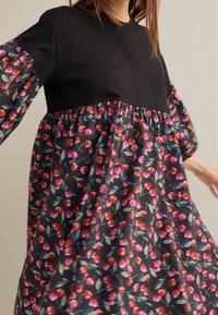 Czarny top z krótkimi rękawami, z kwiecistą spódnicą w czerwone wiśnie i różowymi akcentami na ciemnym tle. Lekka, zwiewna tkanina.