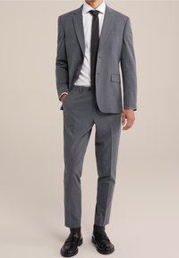 Gray suit with a notched lapel, single-button closure, and slim-fit trousers. Paired with a white shirt and black tie, and loafers.