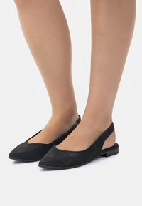 Ballerine nere con cinturino, dalla punta affusolata, realizzate in materiale testurizzato, presentano un design a ritaglio e un tacco basso per il massimo comfort.