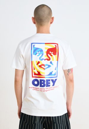 White cotton t-shirt featuring a colorful graphic on the back with faces, patterns, and the word "OBEY" in bold blue. Vertical striped pants.