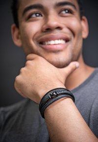Black braided leather bracelet with a textured design, featuring a silver metallic accent. Worn on the wrist of a male model.