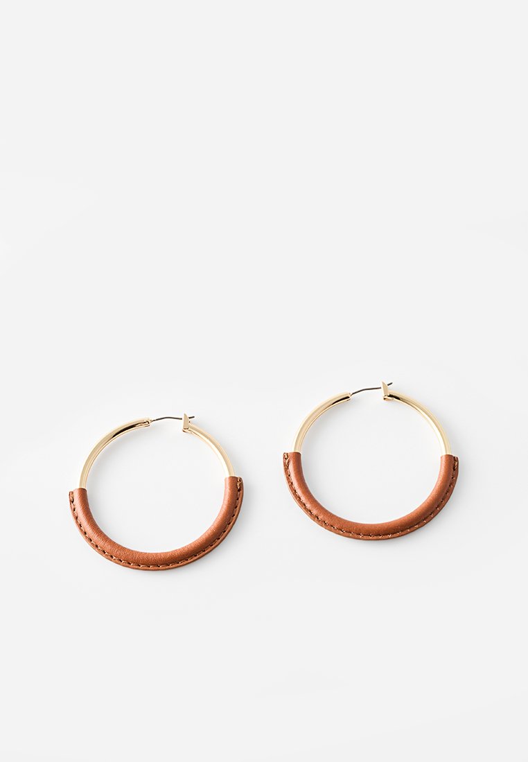 Boucles d'oreilles en or en forme de créole, agrémentées d'une touche de cuir brun incurvé en bas, créant un design bicolore avec une finition métallique lisse.