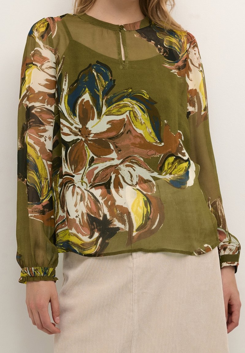 Blouse verte transparente avec motif floral multicolore, encolure ronde, manches longues avec poignets élastiques et détail de bouton à l'encolure.