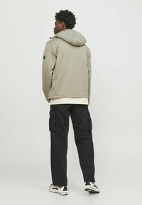 Lichtgrijze hoodie met een gladde textuur, gedragen over een wit shirt, gecombineerd met zwarte cargobroek en witte sneakers.