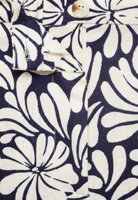 Navy and white floral-patterned fabric featuring a button, zipper detail, and textured surface, showcasing a pronounced design and contrast.