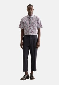 Camicia a maniche corte con bottoni e un vivace motivo floreale, abbinata a pantaloni eleganti scuri e scarpe nere con finitura liscia.