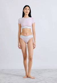 Μωβ κοντό τοπ με λευκή ελαστική ταινία, συνδυασμένο με μαγιό μπικίνι που διαθέτει παρόμοια ταινία, πάνω σε ουδέτερο φόντο.