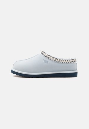 Scarpa slip-on azzurra chiaro con suola scura, bordo decorativo cucito intorno all'apertura e logo UGG sul lato.