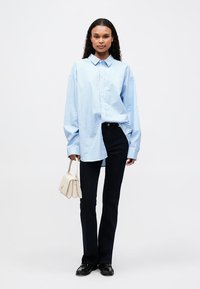 Lys blå stripete oversized skjorte med knapper, mørke jeans, svarte sko og en liten hvit håndveske. Enkel, uformell design med en avslappet passform.