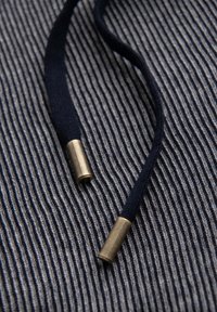 Cordon marin bleu marine avec embouts en métal laiton reposant sur une surface en tissu rayé gris et bleu marine.