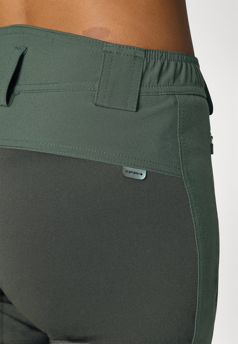Ciemnozielone spodnie sportowe z gładką teksturą, elastycznym pasem i małą metką z logo na bocznej szwie.
