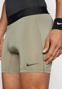 Nike Pro muške kompresijske kratke hlače u maslinastoj boji, s crnim pojasom s logotipom, glatkom teksturom i prilagođenim dizajnom.