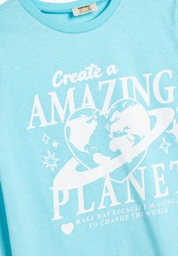 Jasnoniebieska bawełniana koszulka z krótkim rękawem i okrągłym dekoltem, zdobiona białym napisem oraz globusem w sercu, otoczonym gwiazdami i grafikami planet.