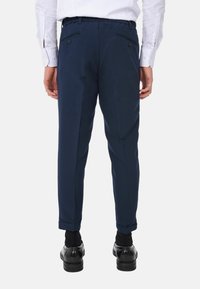 Pantaloni blu navy a gamba affusolata con una finitura testurizzata. Presentano una vita elastica, due tasche posteriori e orli risvoltati.
